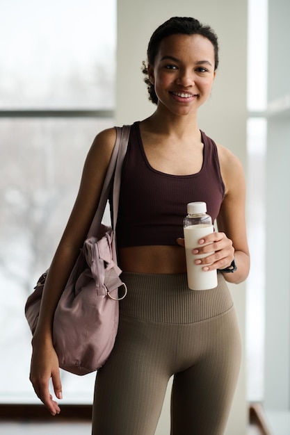 Portrait de jeune fille sportive en vêtements de sport souriant à la caméra en se tenant debout dans la salle de sport