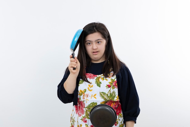 Portrait de jeune fille en tablier coloré tenant une poêle à frire.