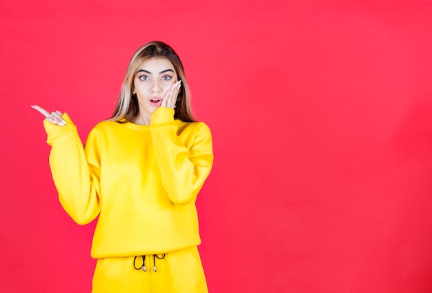 Portrait de jeune fille en tenue jaune debout sur le mur rouge