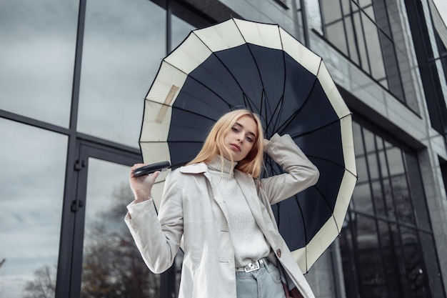 Portrait de jeune fille en trench-coat avec parapluie près du centre d'affaires