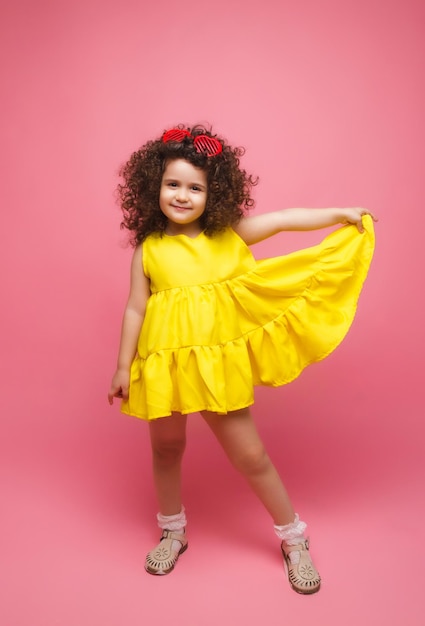 Portrait d'une jeune fille vêtue d'une robe jaune jolie jolie mignonne gaie joyeuse petite fille isolée sur fond rose