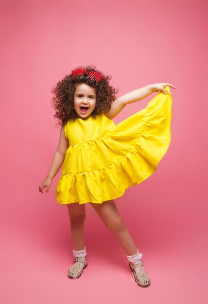 Portrait d'une jeune fille vêtue d'une robe jaune jolie jolie mignonne gaie joyeuse petite fille isolée sur fond rose