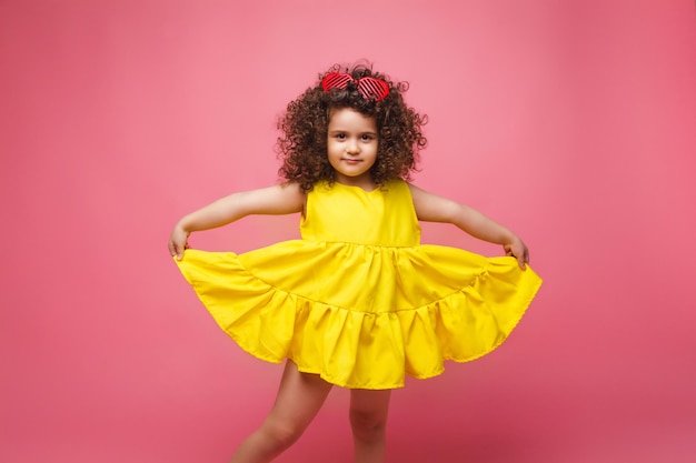 Portrait d'une jeune fille vêtue d'une robe jaune jolie jolie mignonne gaie joyeuse petite fille isolée sur fond rose