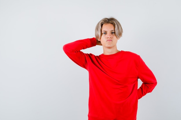 Portrait de jeune garçon adolescent avec la main derrière la tête en pull rouge et à la vue de face concerné