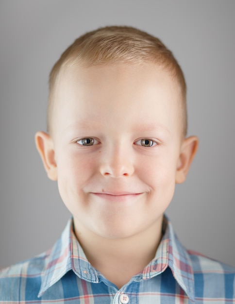 Photo portrait d'un jeune garçon blond sur fond gris. l'enfant sourit et regarde la caméra