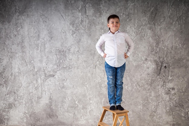 Portrait d'un jeune garçon debout sur une chaise isolée sur fond blanc dans le studio