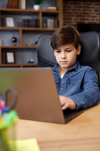 Portrait d'un jeune garçon étudiant à distance à la maison à l'aide d'un ordinateur portable Écolier mignon faisant ses devoirs en regardant un écran d'ordinateur Apprentissage à distance et éducation à domicile Enfance heureuse