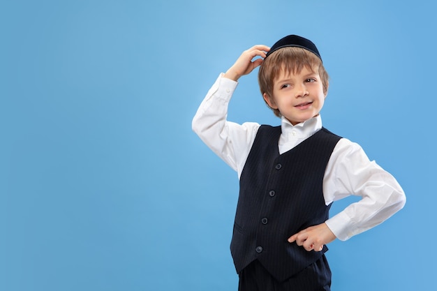Portrait d'un jeune garçon juif orthodoxe isolé sur le mur bleu du studio