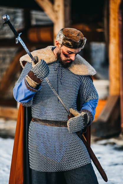 Portrait de jeune guerrier en armure, chapeau et manteau après la bataille. Un homme tient une arme dans ses mains.