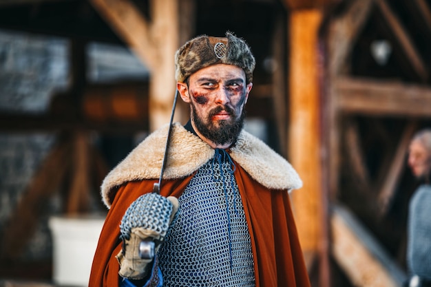 Photo portrait de jeune guerrier en armure, chapeau et manteau après la bataille. un homme tient une arme dans ses mains.