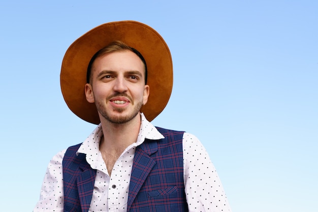 Portrait d'un jeune homme adulte dans une chemise blanche de chapeau et un gilet sur le fond d'un paysage naturel