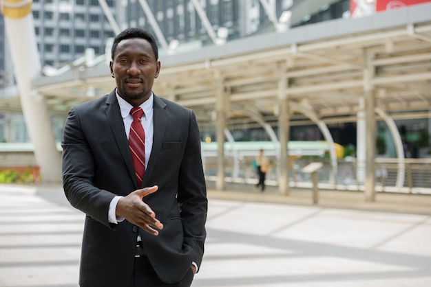 Portrait de jeune homme d'affaires africain beau en costume contre vue du bâtiment moderne dans la ville en plein air