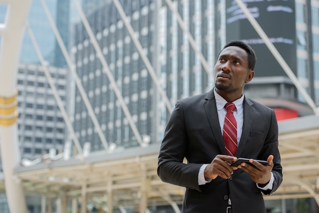 Portrait de jeune homme d'affaires africain beau en costume contre vue du bâtiment moderne dans la ville en plein air