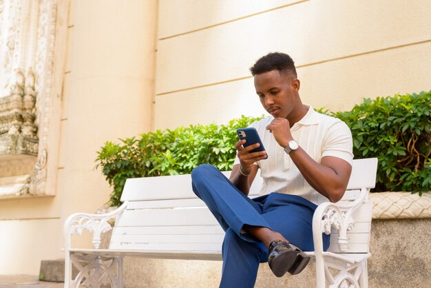 Portrait de jeune homme d'affaires africain portant des vêtements décontractés et utilisant un téléphone portable en position assise