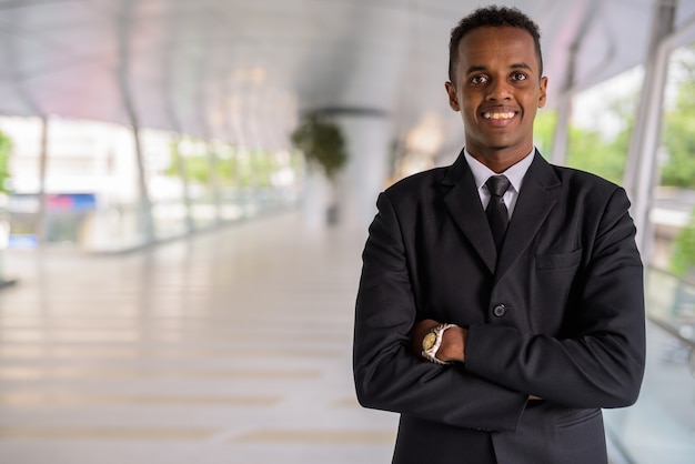 Portrait de jeune homme d'affaires africain prospère souriant à l'extérieur avec les bras croisés