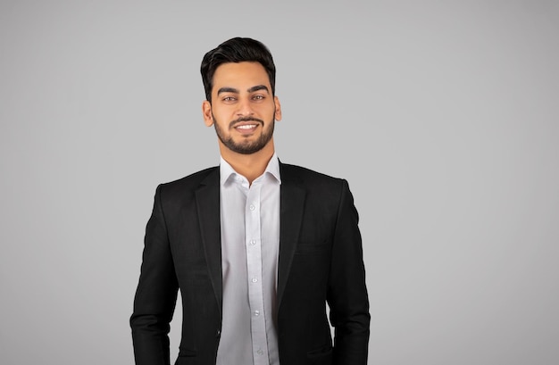 Portrait de jeune homme d'affaires arabe souriant en costume debout sur fond gris