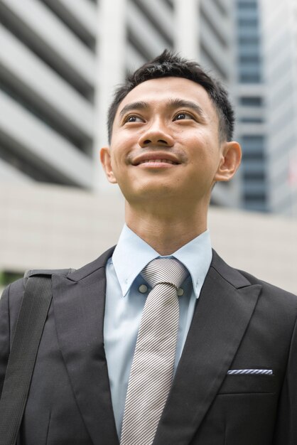 Photo portrait d'un jeune homme d'affaires asiatique tenant une mallette à la main isolée sur la ville