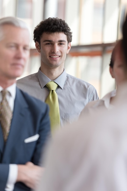 portrait d'un jeune homme d'affaires aux cheveux bouclés et à l'intérieur d'un bureau moderne et lumineux avec de grandes fenêtres en arrière-plan et un groupe de personnes devant