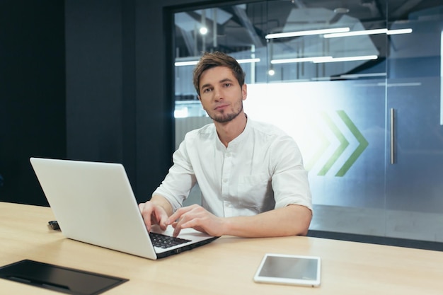 Portrait de jeune homme d'affaires avec barbe homme travaillant dans un bureau moderne avec ordinateur portable souriant et regardant la caméra