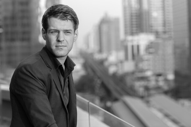 Portrait de jeune homme d'affaires beau en costume contre vue sur la ville en noir et blanc