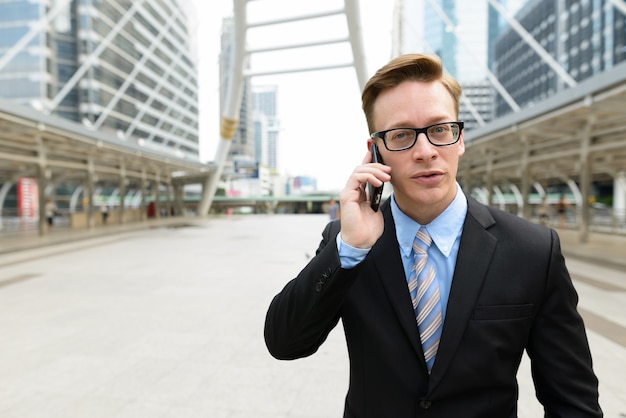 Portrait de jeune homme d'affaires blond beau en costume au pont de skywalk dans la ville en plein air