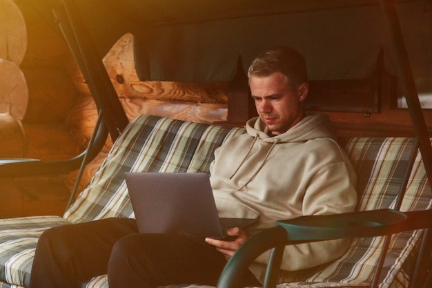 Portrait De Jeune Homme D'affaires Branché Avec Terrasse Extérieure Pour Ordinateur Portable De Maison De Campagne. Homme Bourreau De Travail Dans Des Vêtements Décontractés à La Maison Travaillant En Vacances. Inspiration Créative Et Création D'entreprise. Espace De Copie