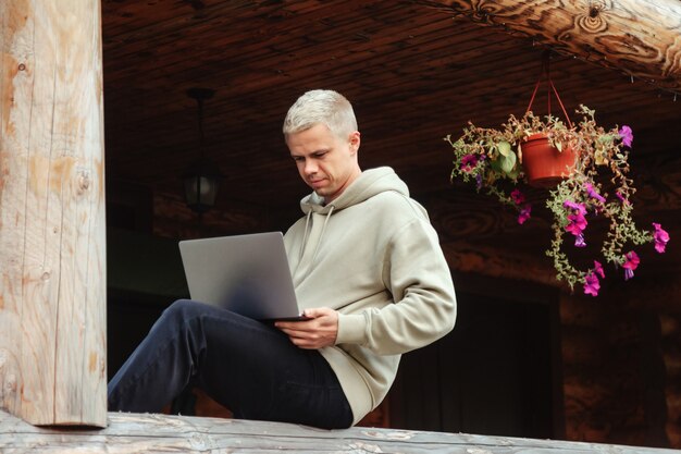 Portrait de jeune homme d'affaires branché avec terrasse extérieure pour ordinateur portable de maison de campagne. Homme bourreau de travail dans des vêtements décontractés à la maison travaillant en vacances. Inspiration créative et création d'entreprise. Espace de copie