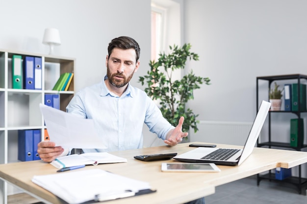 Portrait d'un jeune homme d'affaires économiste gestionnaire travaillant au bureau au bureau sur un ordinateur portable travaillant avec des papiersdocuments