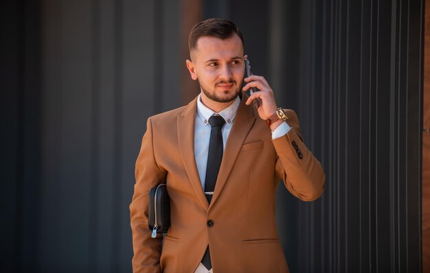 Photo portrait d'un jeune homme d'affaires heureux portant un costume brun près du bâtiment de bureaux moderne