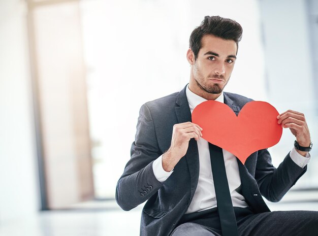 Portrait d'un jeune homme d'affaires à la mode posant avec un coeur en papier au bureau