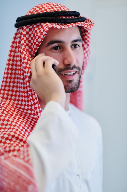Photo portrait de jeune homme d'affaires musulman à l'aide de téléphone portable. garçon arabe réussi dans des vêtements traditionnels représentant la technologie