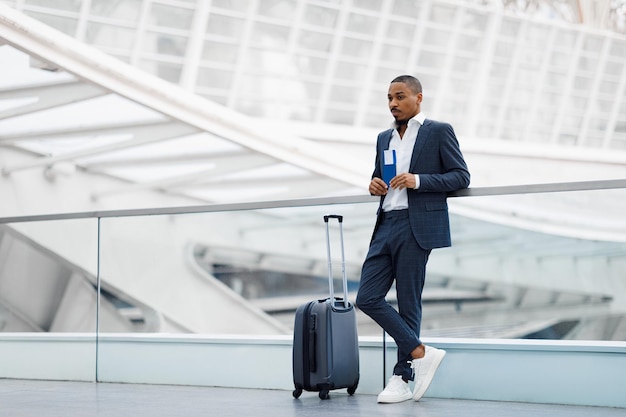 Photo portrait de jeune homme d'affaires noir avec valise en attente à l'aéroport