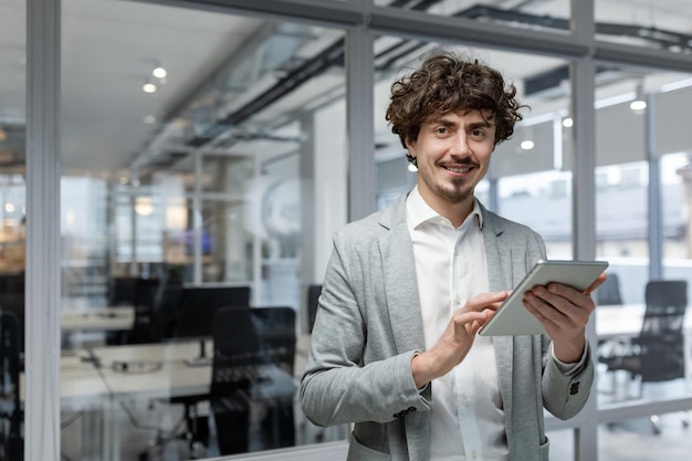 Portrait d'un jeune homme d'affaires prospère avec une tablette dans les mains en souriant et en regardant