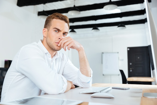 Portrait d'un jeune homme d'affaires réfléchi travaillant avec un ordinateur au bureau