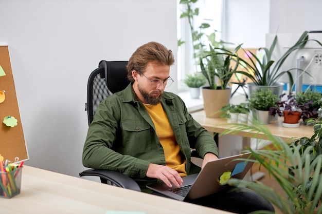 Portrait d'un jeune homme d'affaires séduisant utilisant un ordinateur portable dans un bureau moderne en tapant sur un ordinateur portable