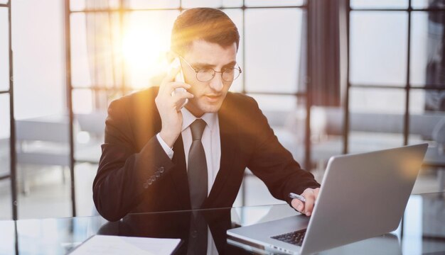 Portrait d'un jeune homme d'affaires sérieux dans un bureau décontracté appelant au téléphone tout en travaillant avec un ordinateur portable