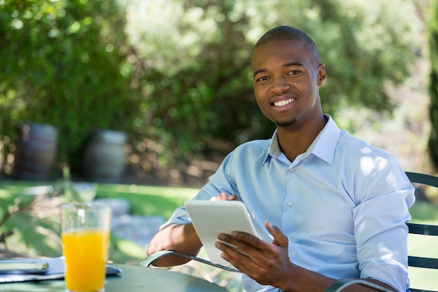 Portrait de jeune homme d'affaires souriant à l'aide de tablette numérique au restaurant en plein air