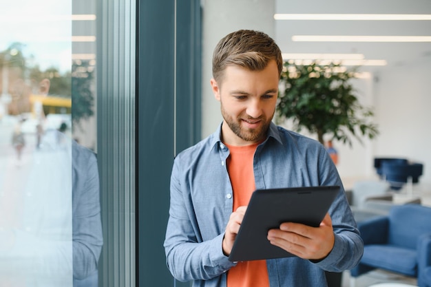 Portrait de jeune homme d'affaires avec tablette debout dans un bureau travaillant