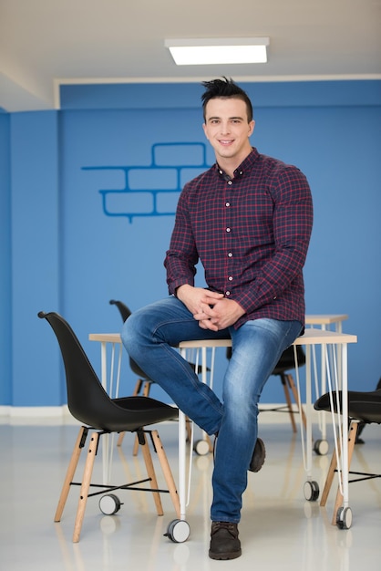 portrait d'un jeune homme d'affaires en vêtements décontractés assis sur une table dans un nouvel espace de bureau de démarrage