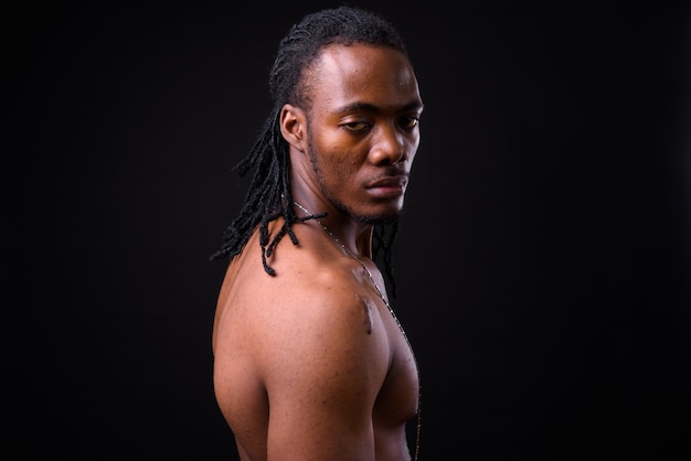 Portrait de jeune homme africain beau avec des dreadlocks torse nu sur fond noir