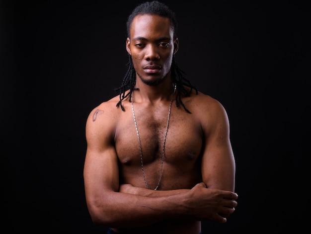 Portrait de jeune homme africain beau avec des dreadlocks torse nu sur fond noir