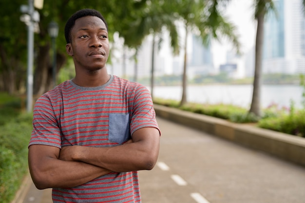 Portrait de jeune homme africain beau se détendre dans le parc et penser