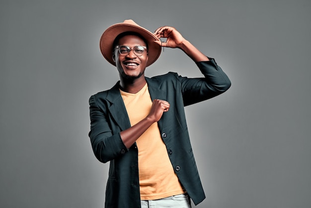 Portrait d'un jeune homme africain en chapeau et veste dansant sur fond gris Espace de copie