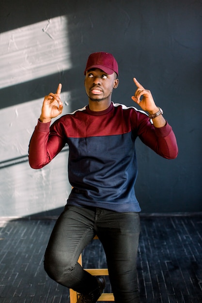 Portrait de jeune homme africain excité avec les bras tendus et riant vêtu d'un pull en molleton rouge et bonnet rouge