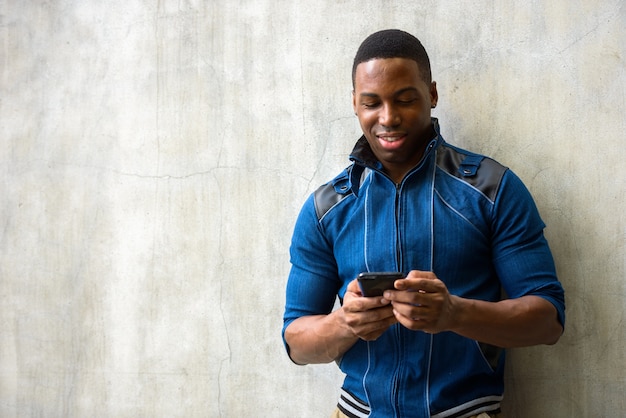 Portrait de jeune homme africain musclé beau vêtu d'une veste bleue contre le mur de béton à l'extérieur