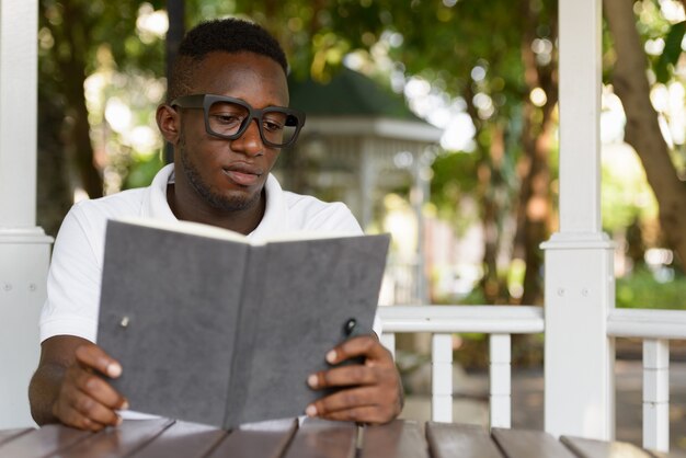 Portrait de jeune homme africain nerd en tant qu'étudiant avec des lunettes dans le parc en plein air