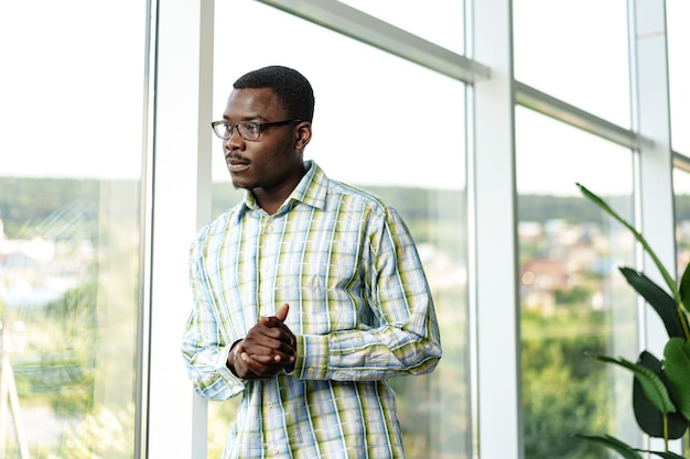 Portrait d'un jeune homme africain réfléchi dans des lunettes debout près de la fenêtre