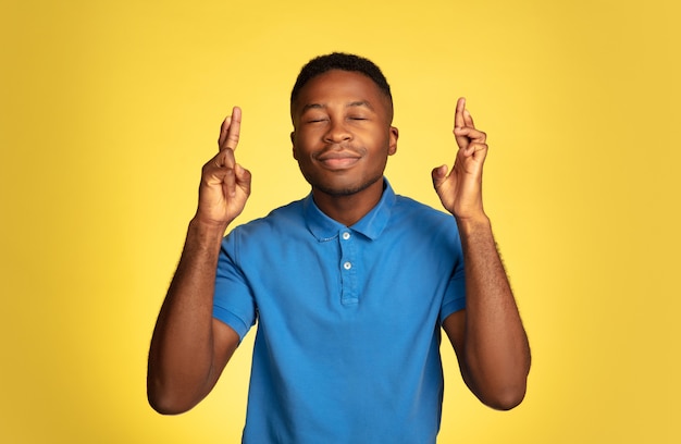 Portrait de jeune homme afro-américain isolé sur fond de studio jaune, expression faciale.