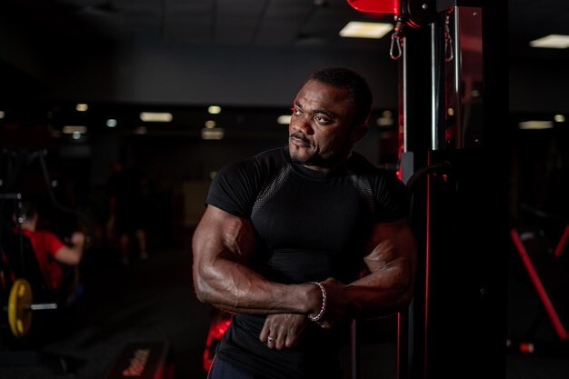 Portrait de jeune homme afro-américain musclé en vêtements de sport regardant de côté tout en posant sur fond de gym. Sport, entraînement, concept de musculation.