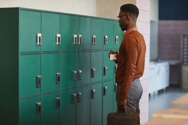 Portrait de jeune homme afro-américain ouvrant le casier au collège ou immeuble de bureaux, espace copie